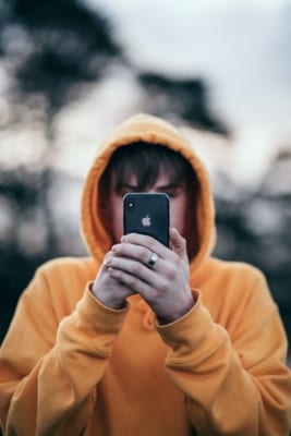 En gutt i gul hettegenser som holder en mobil foran ansiktet sitt